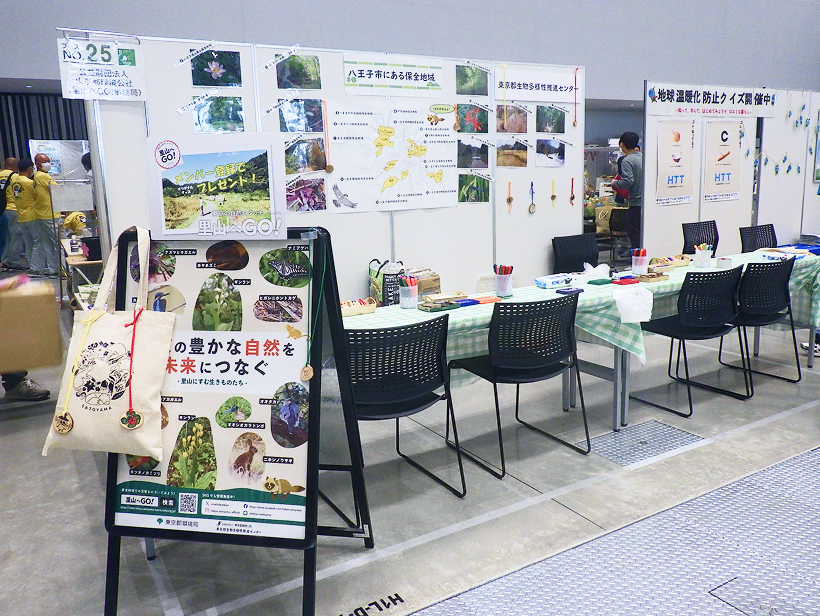 自然保護や環境保全をテーマにしたイベントの展示ブース。壁面には八王子市の保全地域に関するパネルが貼られ、手前にはワークショップ用のテーブルが並んでいます。