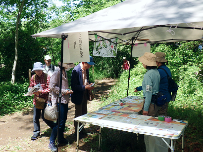 緑豊かな屋外に設置されたテントの下で、「ミニ自然観察会」の受付を行っている様子。