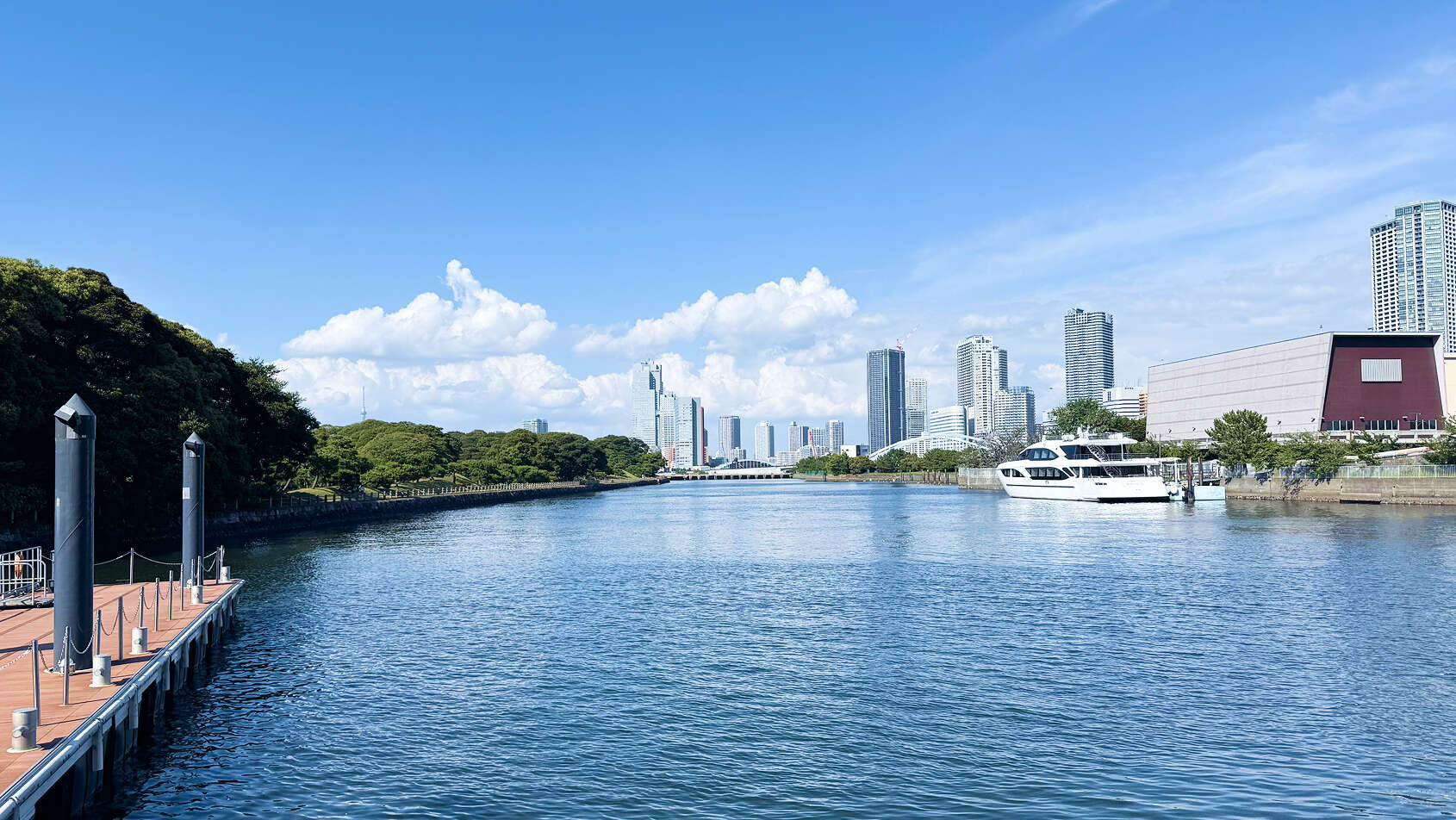 青空の下、高層ビル群を背景に流れる広い運河の風景