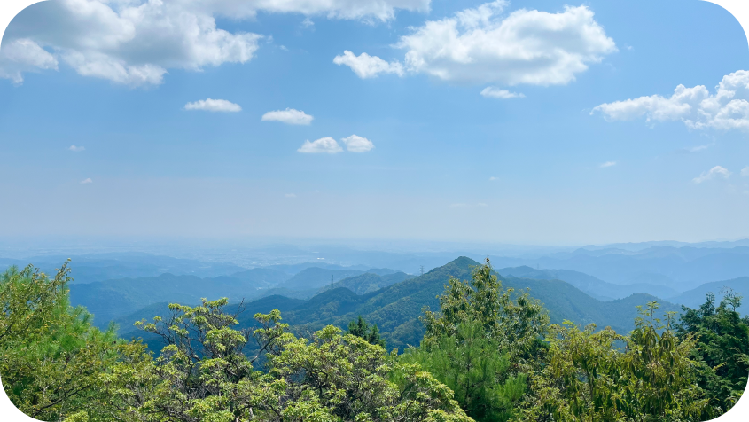 青空と白い雲の下、遠くまで連なる緑豊かな山々のパノラマ風景
