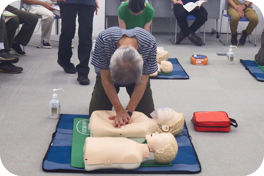 講習会場にて、訓練用の人形（マネキン）を使用して胸骨圧迫（心臓マッサージ）の練習を行う参加者の様子。