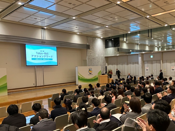 「第1回 Tokyo-NbS アクションアワード」の会場風景。前方のスクリーンにイベント名が表示され、多くの観客が座席からステージを見守っている様子。